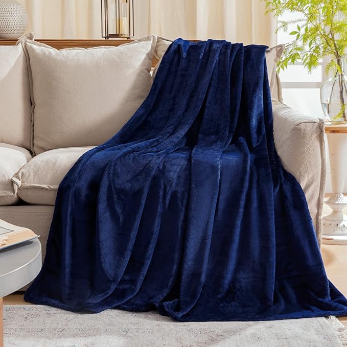 A luxurious navy blue fleece blanket draped over a beige sofa in a cozy, well-lit living room. no-save