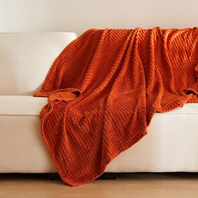 A plush burnt orange fleece blanket with a textured pattern draped over a cream-colored sofa, adding warmth and coziness to the space. no-save