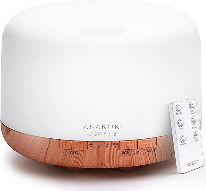A modern essential oil diffuser with a white top and wood-grain base, featuring control buttons and a remote control beside it. no-save