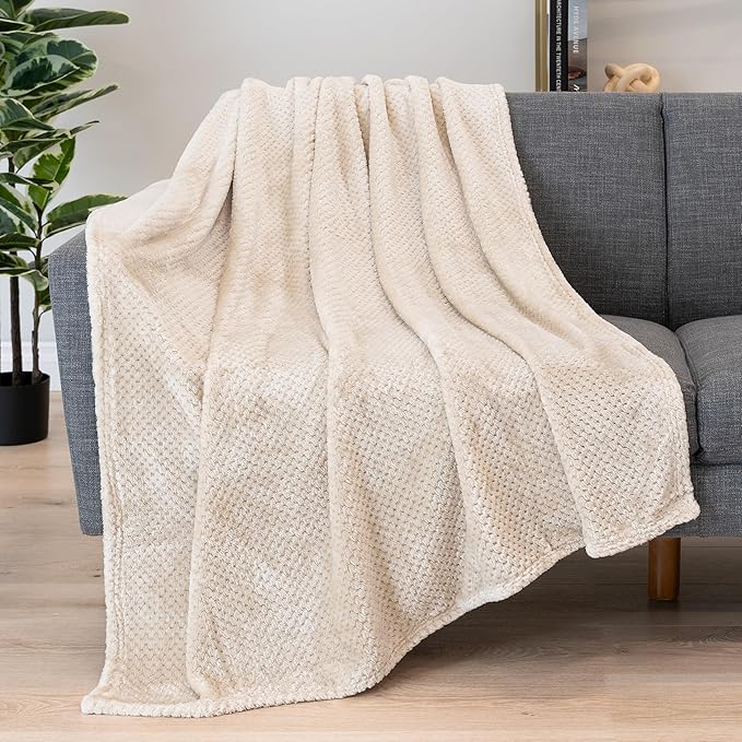 Soft and plush beige throw blanket draped over a gray sofa, adding warmth and elegance to the space. no-save