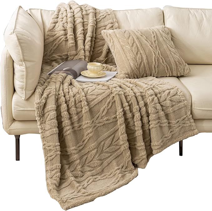 A cozy tan throw blanket with a textured leaf pattern draped elegantly over a cream-colored sofa, paired with a matching decorative pillow. A cup of tea and an open book rest nearby, creating a warm and inviting atmosphere perfect for relaxation.  no-save