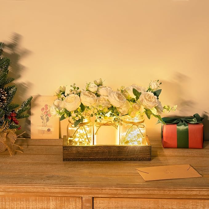 Elegant centerpiece featuring illuminated mason jars filled with fairy lights and white artificial roses, placed in a wooden tray on a cozy, festive tabletop setting. no-save