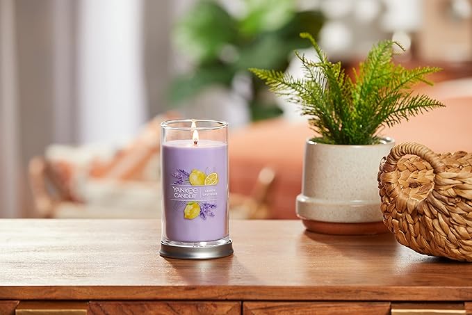 Lit lavender and lemon-scented Yankee Candle in a glass jar, placed on a wooden surface alongside a potted green plant and woven decor, creating a cozy and refreshing ambiance. no-save