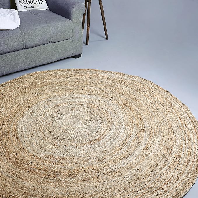Round woven jute rug with a natural texture, placed in a modern living space next to a gray sofa, adding warmth and an earthy touch to the decor. no-save